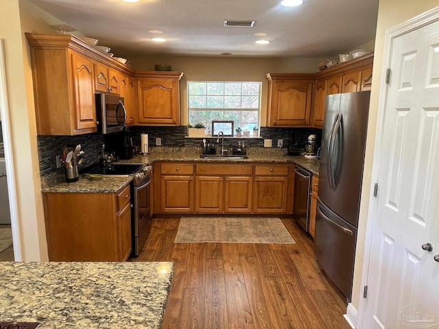 kitchen featuring appliances with stainless steel finishes, tasteful backsplash, sink, dark stone countertops, and dark hardwood / wood-style floors