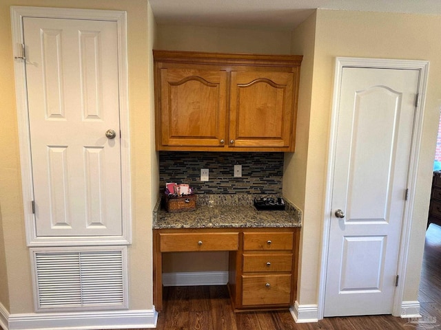 bar with stone countertops, dark hardwood / wood-style flooring, built in desk, and tasteful backsplash