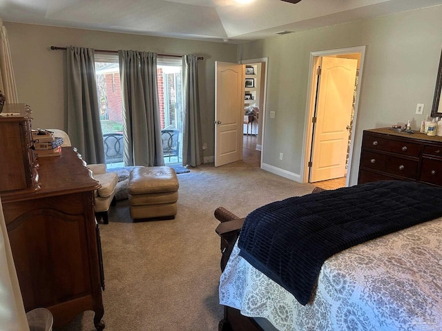 bedroom with a tray ceiling, light colored carpet, and access to outside