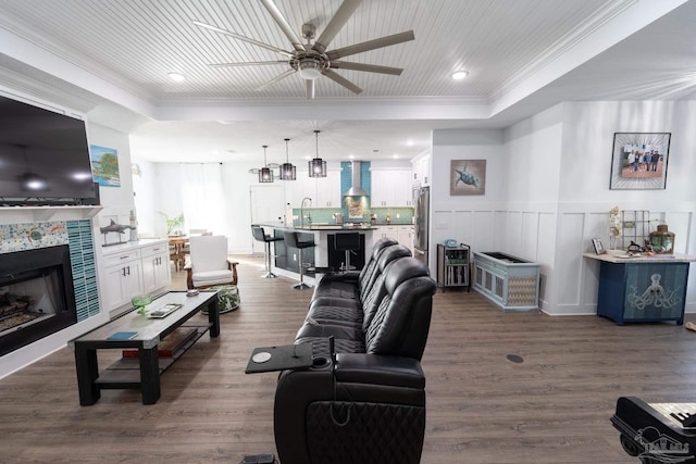 living room with ceiling fan, a fireplace, ornamental molding, and dark wood-type flooring