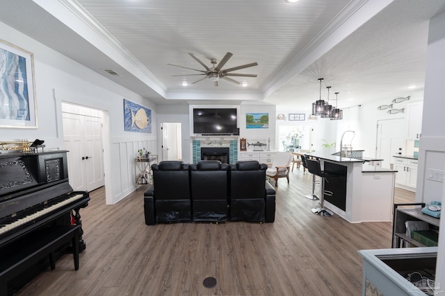 living room featuring ornamental molding, a tray ceiling, ceiling fan, dark hardwood / wood-style floors, and a stone fireplace