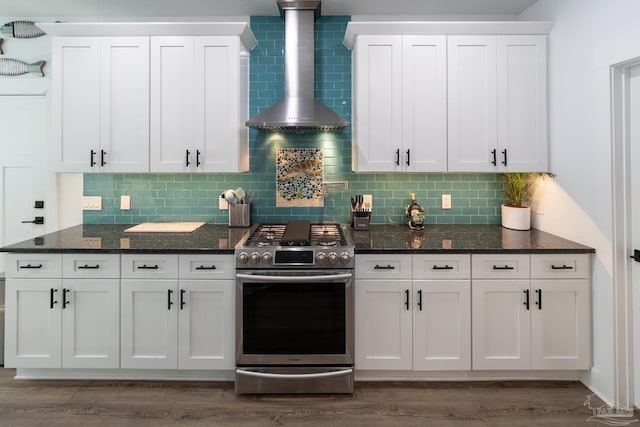 kitchen featuring white cabinetry, wall chimney range hood, stainless steel gas range oven, backsplash, and dark stone counters