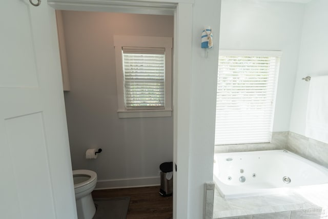 bathroom with hardwood / wood-style floors, toilet, and tiled tub