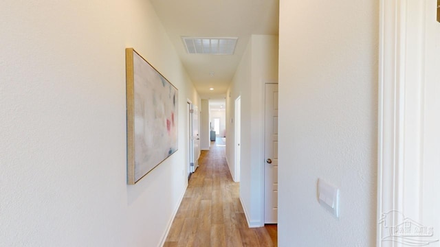 hallway with light wood finished floors, visible vents, and baseboards