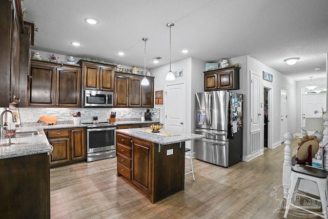 kitchen with stainless steel appliances, a sink, a kitchen island, decorative backsplash, and a breakfast bar