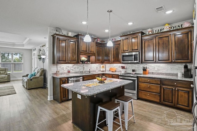 kitchen featuring appliances with stainless steel finishes, a kitchen island, open floor plan, a sink, and dark brown cabinetry