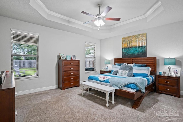 carpeted bedroom with a raised ceiling, crown molding, a ceiling fan, and baseboards