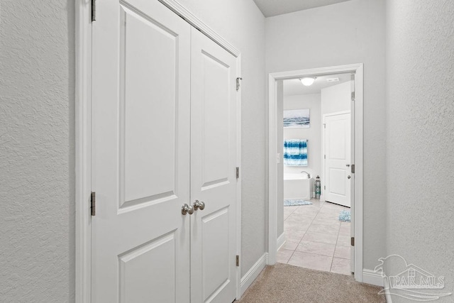 corridor with a textured wall, light colored carpet, baseboards, and light tile patterned flooring