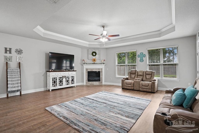 living room featuring a raised ceiling, a ceiling fan, wood finished floors, a tile fireplace, and crown molding