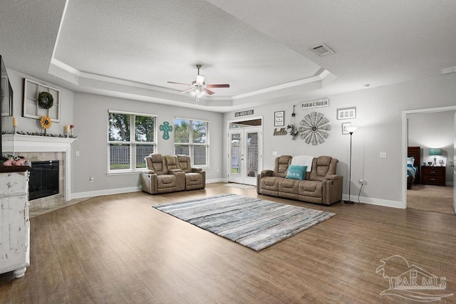 living area with a raised ceiling, a ceiling fan, wood finished floors, baseboards, and a textured ceiling