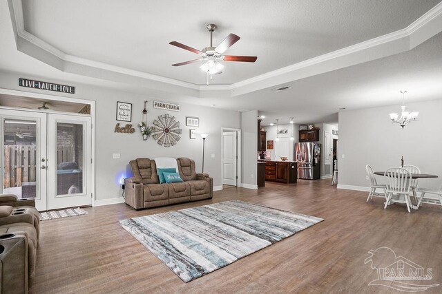 living area with a tray ceiling, crown molding, ceiling fan, dark wood-style floors, and a chandelier