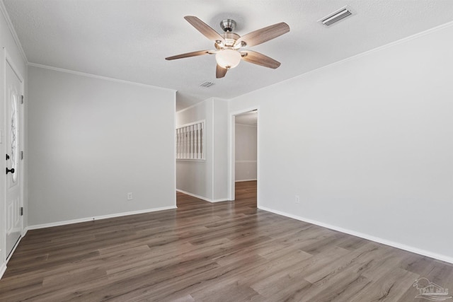 spare room with a ceiling fan, wood finished floors, crown molding, and visible vents