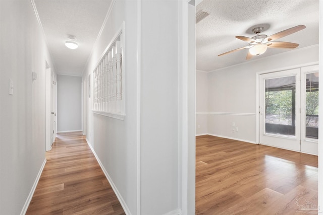 corridor featuring wood finished floors, ornamental molding, and a textured ceiling