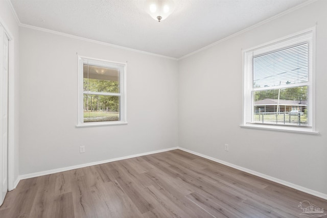 spare room featuring wood finished floors, crown molding, baseboards, and a wealth of natural light