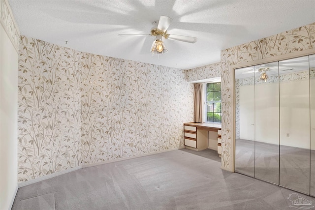 unfurnished bedroom featuring wallpapered walls, carpet floors, a textured ceiling, and ceiling fan