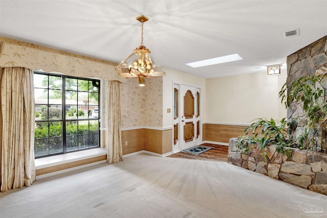 unfurnished dining area featuring wainscoting, visible vents, a skylight, wallpapered walls, and carpet floors
