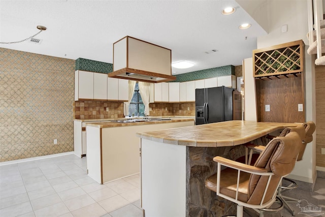 kitchen with a peninsula, white cabinetry, stainless steel gas stovetop, black fridge with ice dispenser, and wallpapered walls
