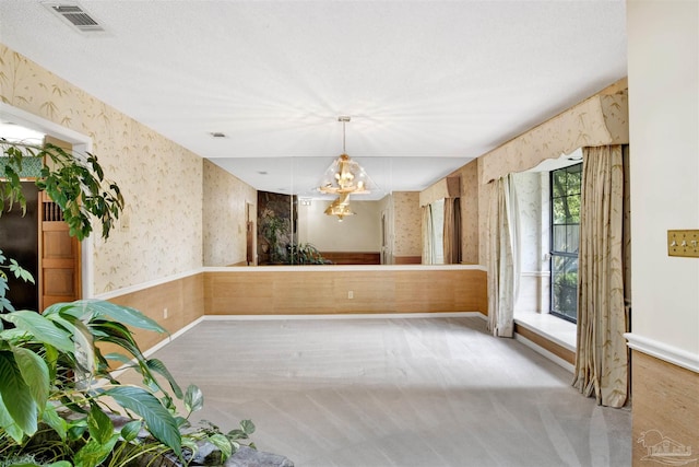 unfurnished dining area featuring wallpapered walls, an inviting chandelier, carpet, baseboards, and visible vents
