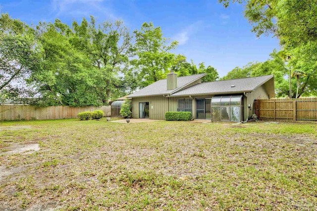 rear view of house featuring a chimney, a fenced backyard, a yard, a patio area, and a sunroom