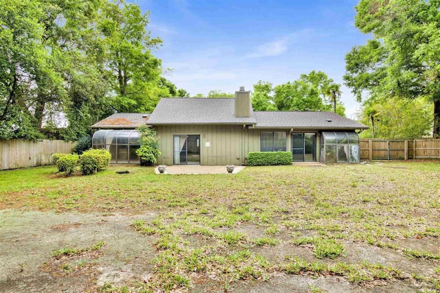 rear view of house featuring a sunroom, a chimney, a fenced backyard, and a greenhouse