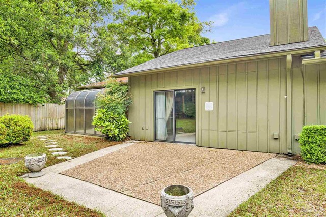 rear view of property featuring a chimney, fence, a shingled roof, board and batten siding, and a patio