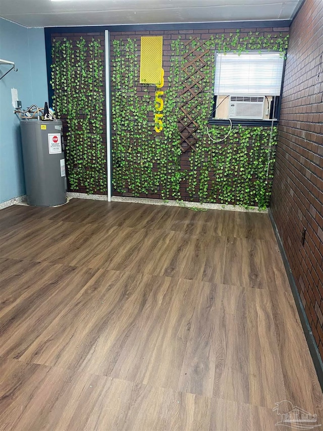 empty room with cooling unit, brick wall, hardwood / wood-style floors, and electric water heater