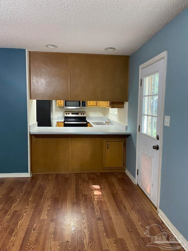 kitchen featuring dark hardwood / wood-style floors, sink, kitchen peninsula, appliances with stainless steel finishes, and a textured ceiling