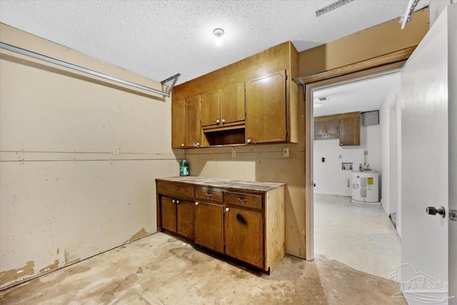 kitchen with brown cabinetry, light countertops, a textured ceiling, water heater, and concrete flooring
