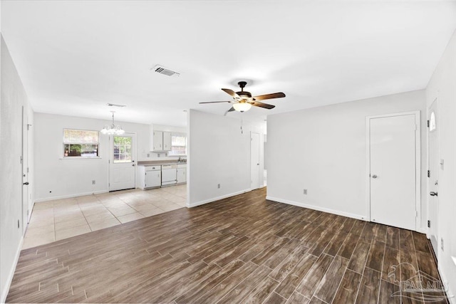 unfurnished living room featuring a chandelier, a ceiling fan, light wood-type flooring, and baseboards