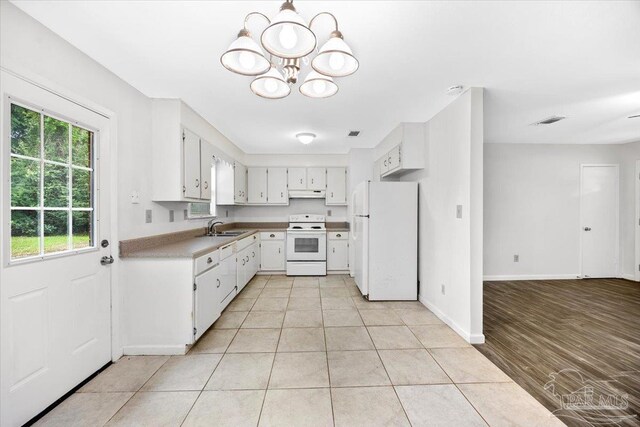 kitchen featuring white appliances, under cabinet range hood, a sink, a chandelier, and white cabinetry