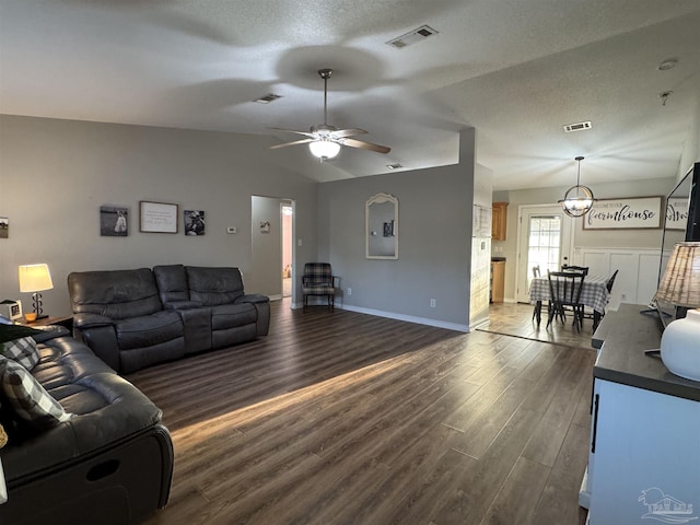 living area featuring visible vents, dark wood-style floors, baseboards, vaulted ceiling, and ceiling fan with notable chandelier