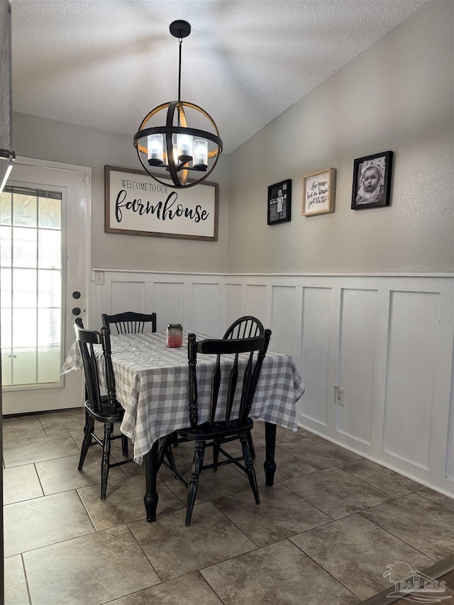 dining area featuring an inviting chandelier, a textured ceiling, lofted ceiling, and a decorative wall