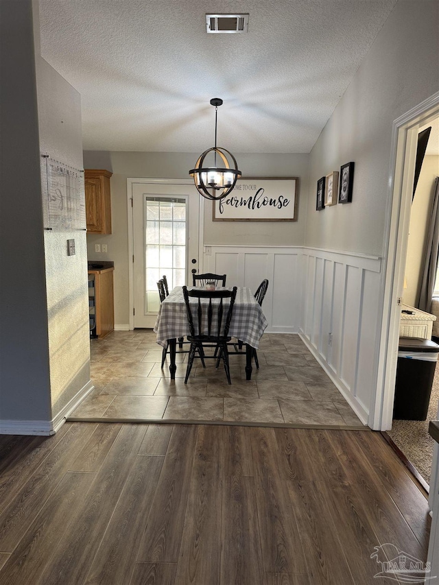 dining room featuring an inviting chandelier, wainscoting, dark wood-style flooring, visible vents, and a textured ceiling