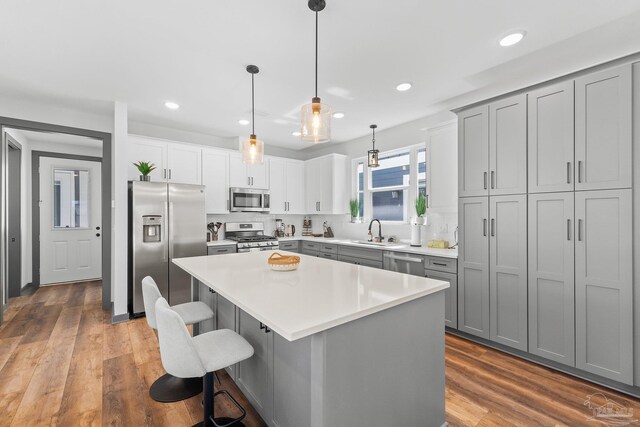 kitchen with sink, appliances with stainless steel finishes, hanging light fixtures, wood-type flooring, and a kitchen island