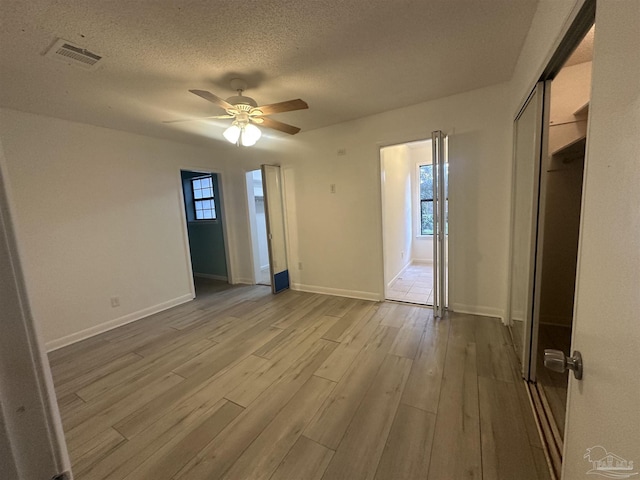 spare room featuring ceiling fan, a wealth of natural light, a textured ceiling, and light wood-type flooring