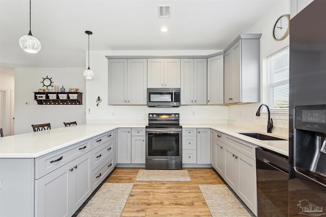 kitchen with kitchen peninsula, appliances with stainless steel finishes, a kitchen breakfast bar, sink, and decorative light fixtures