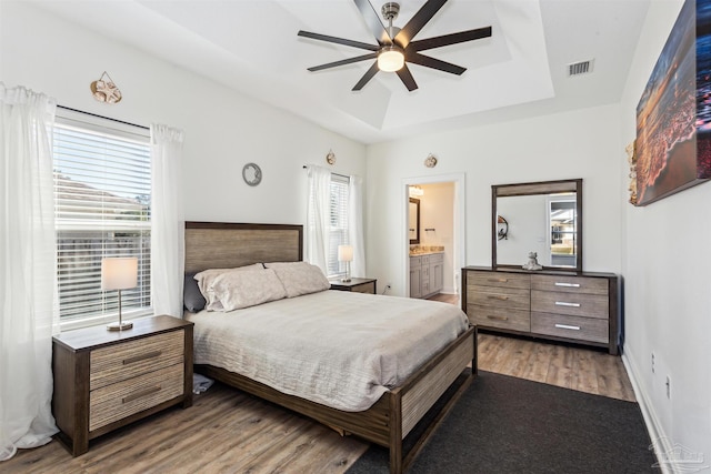 bedroom with hardwood / wood-style floors, ensuite bath, a raised ceiling, and ceiling fan