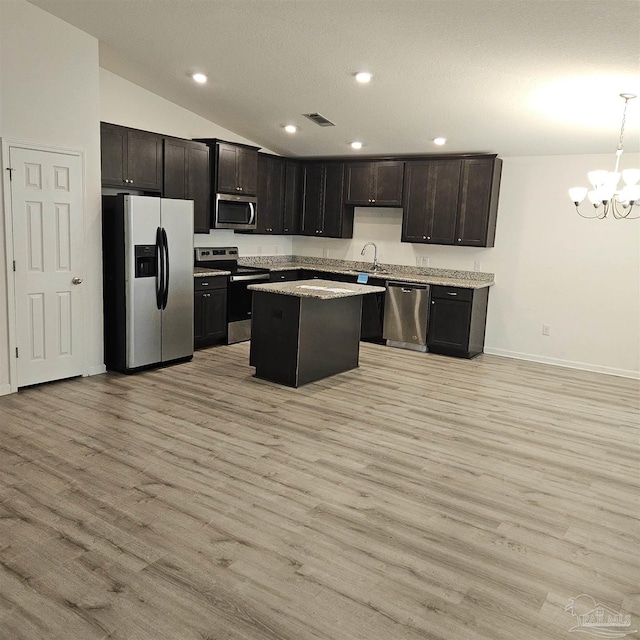 kitchen with lofted ceiling, hanging light fixtures, light wood-type flooring, a kitchen island, and stainless steel appliances