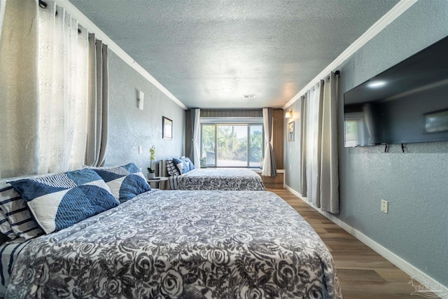 bedroom with baseboards, a textured wall, ornamental molding, wood finished floors, and a textured ceiling