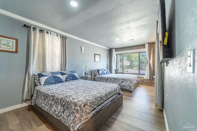 bedroom featuring crown molding, visible vents, a textured wall, wood finished floors, and baseboards