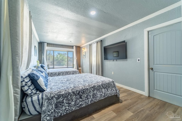 bedroom featuring a textured ceiling, ornamental molding, wood finished floors, and a textured wall