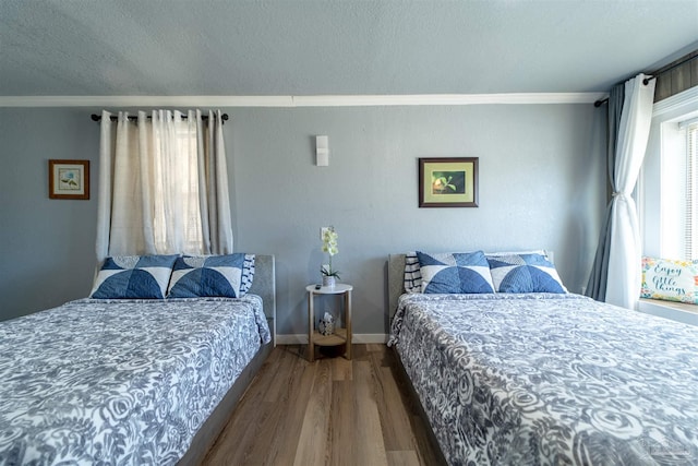 bedroom with baseboards, a textured ceiling, wood finished floors, and crown molding