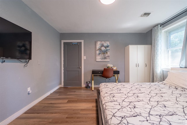 bedroom with baseboards, visible vents, and wood finished floors