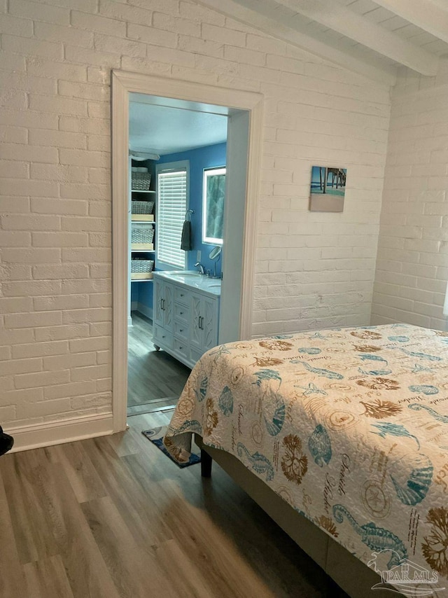 bedroom featuring brick wall, dark wood finished floors, beam ceiling, a sink, and baseboards