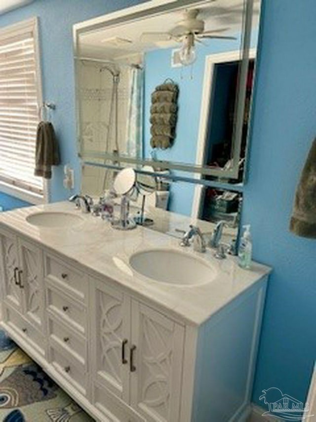bathroom featuring a sink, ceiling fan, double vanity, and a shower