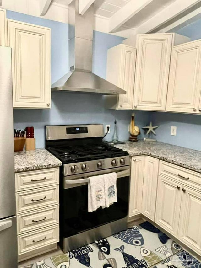 kitchen featuring wall chimney range hood, light stone countertops, appliances with stainless steel finishes, and beam ceiling