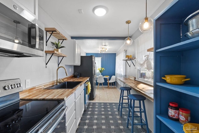 kitchen featuring butcher block counters, stainless steel appliances, hanging light fixtures, white cabinets, and sink