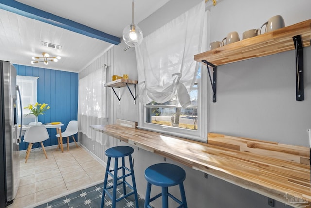 interior space featuring wood counters, a kitchen bar, tile patterned floors, hanging light fixtures, and stainless steel refrigerator