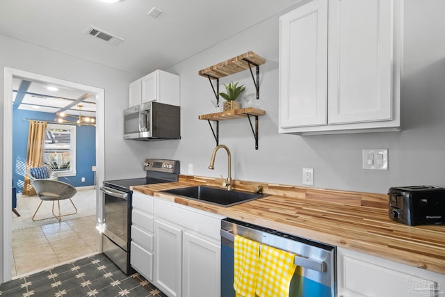 kitchen with wooden counters, sink, dark tile patterned floors, appliances with stainless steel finishes, and white cabinets