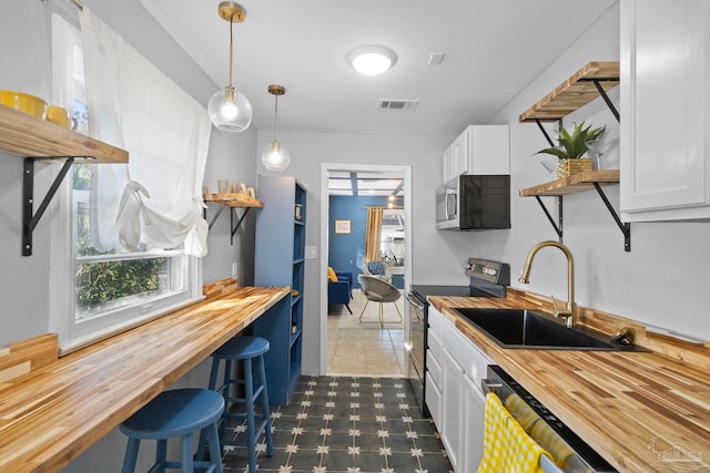 kitchen featuring white cabinets, stainless steel appliances, sink, hanging light fixtures, and butcher block countertops